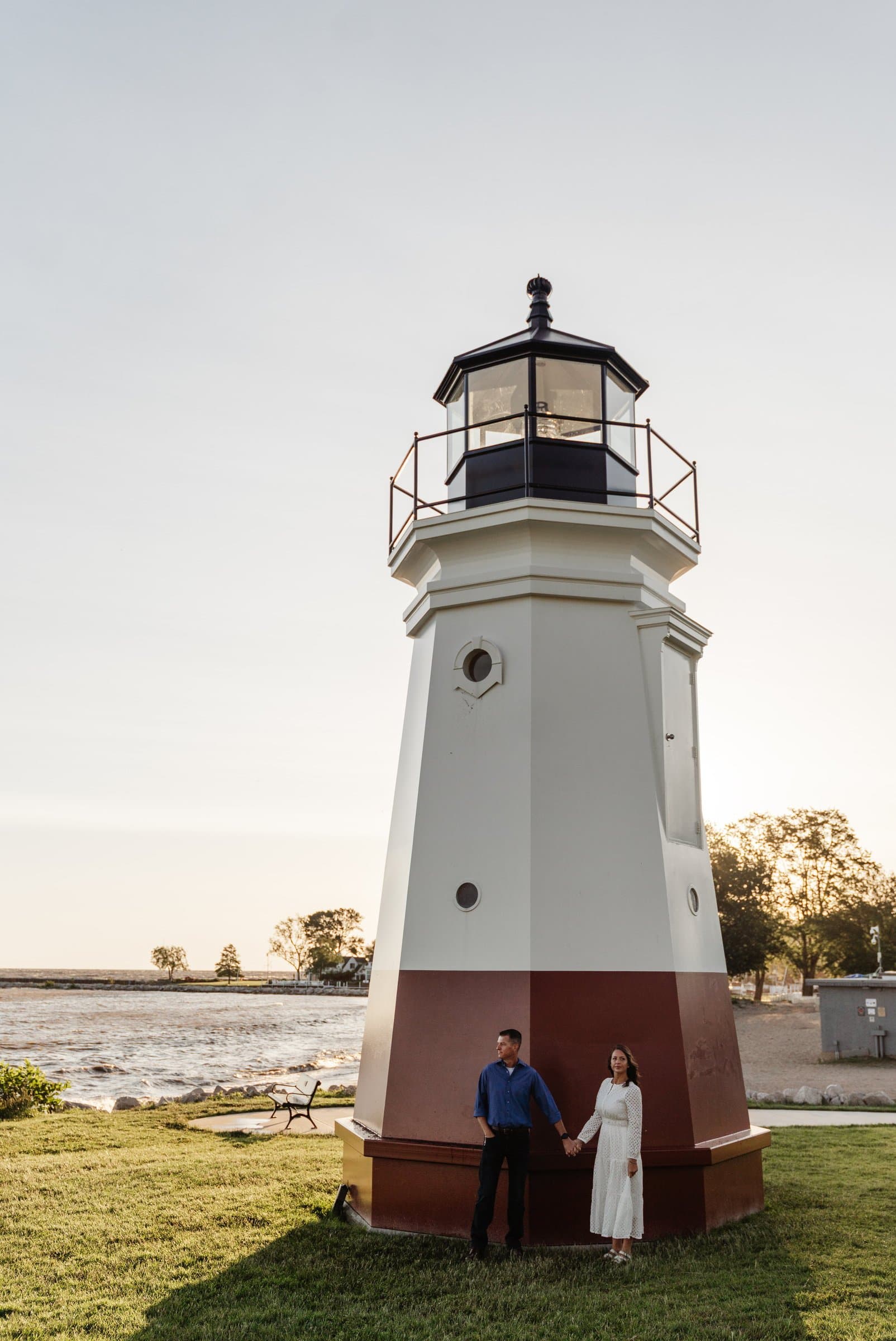 Engaged couple beside a red and white lighthouse on the Lake Erie shoreline