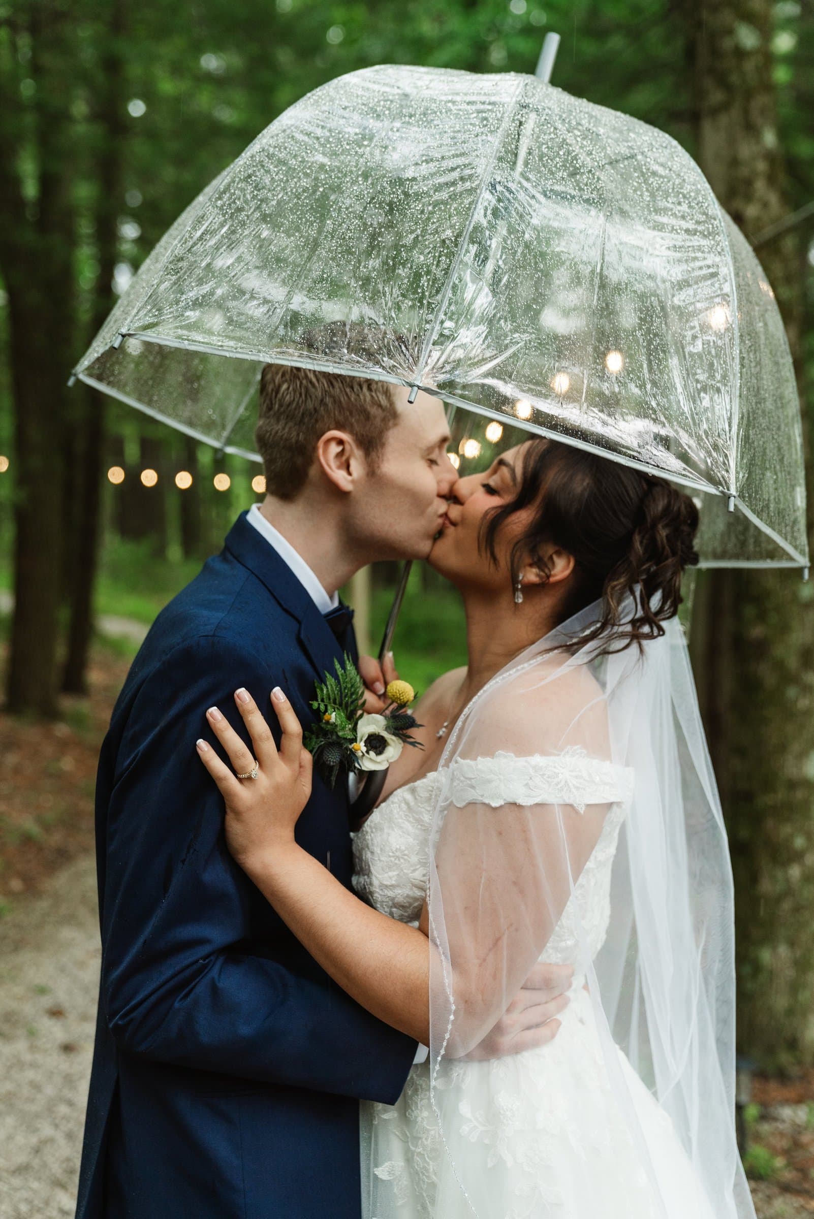Bride and groom kissing under a clear umbrella on a rainy wedding day
