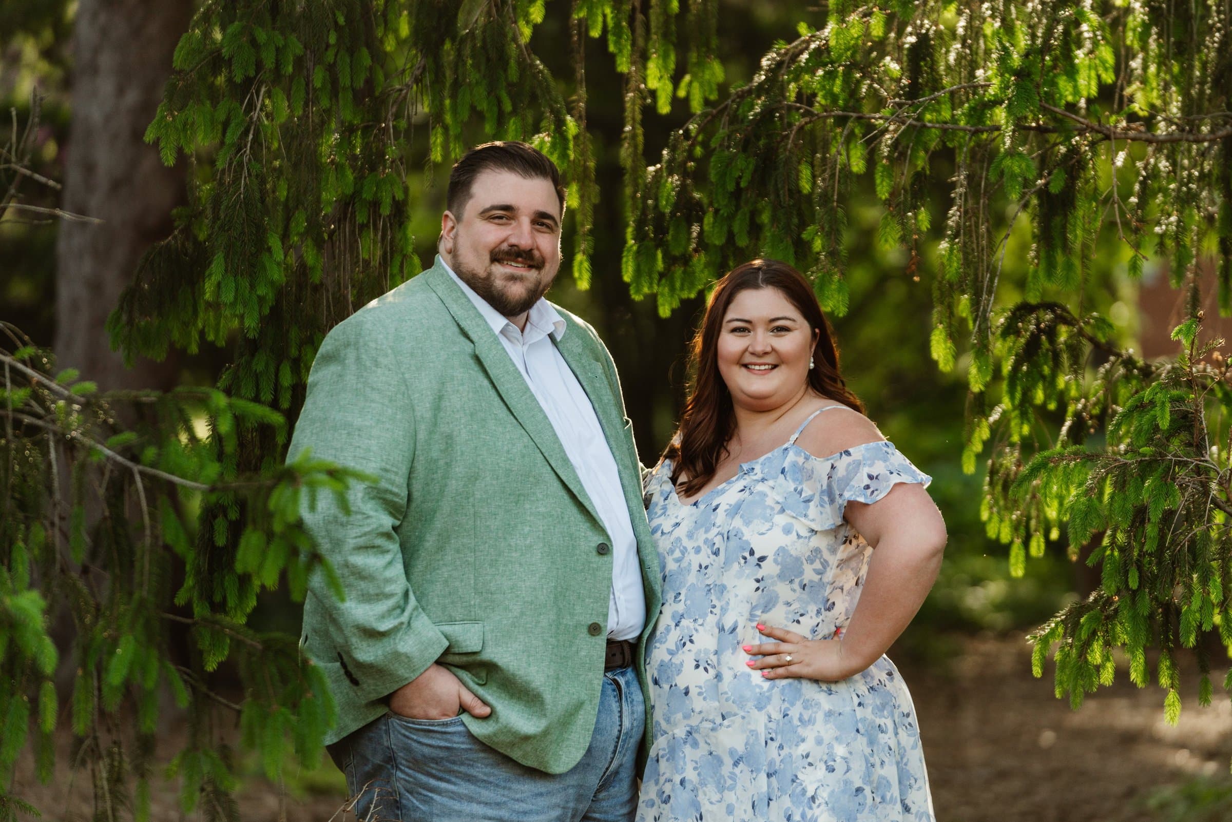 Engaged couple in coordinated sage green and blue floral outfits under a weeping tree
