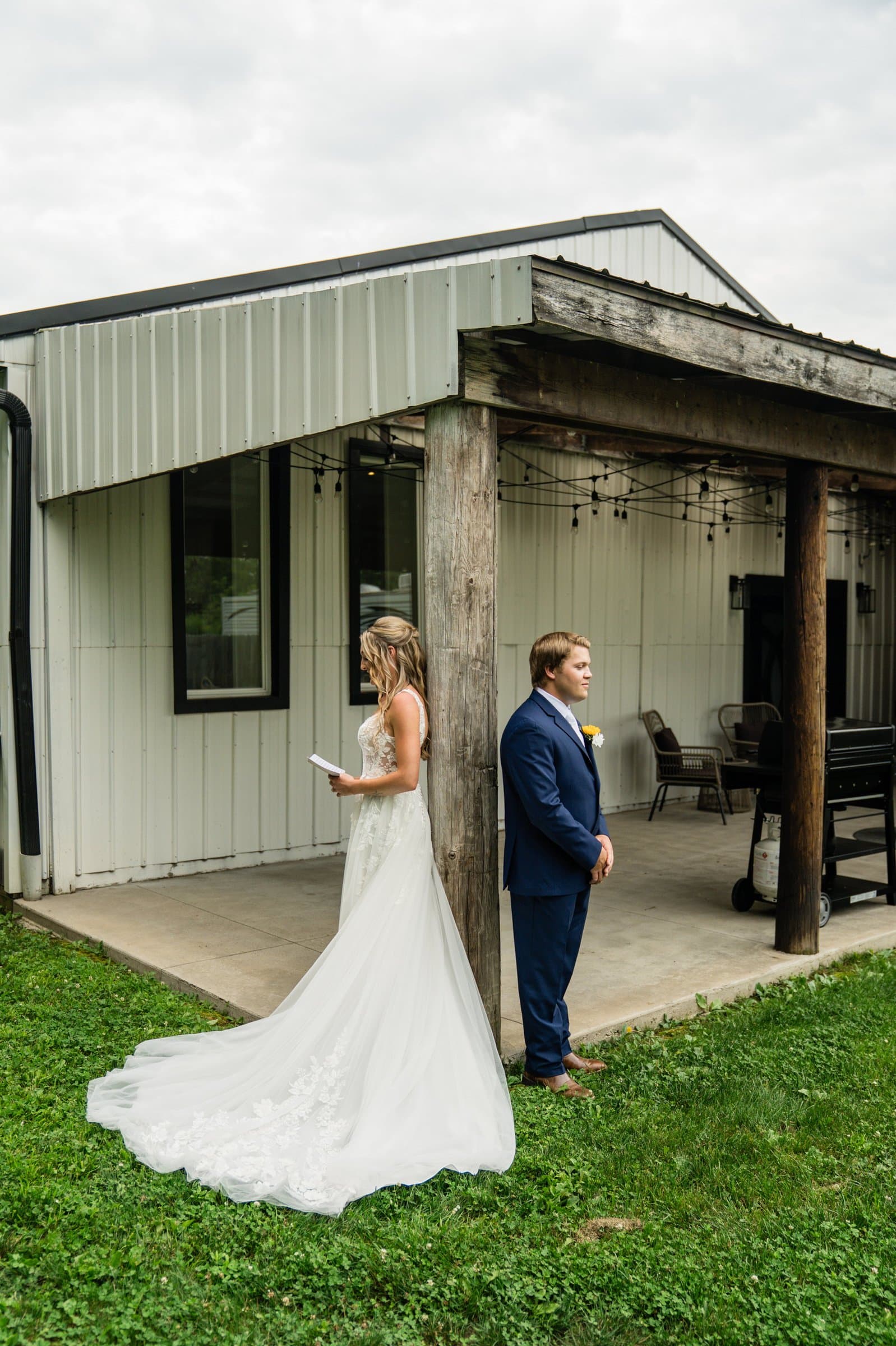 Bride walking up behind her groom for their first look outside a white barn