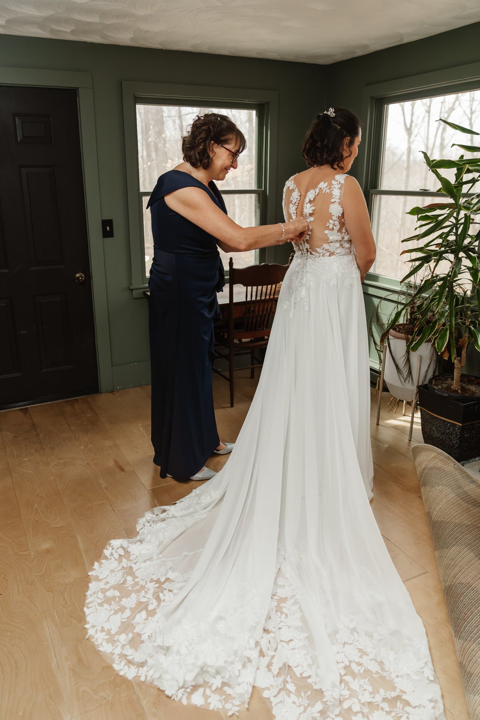 Mother of the bride fastening the back of the wedding dress beside a bright window