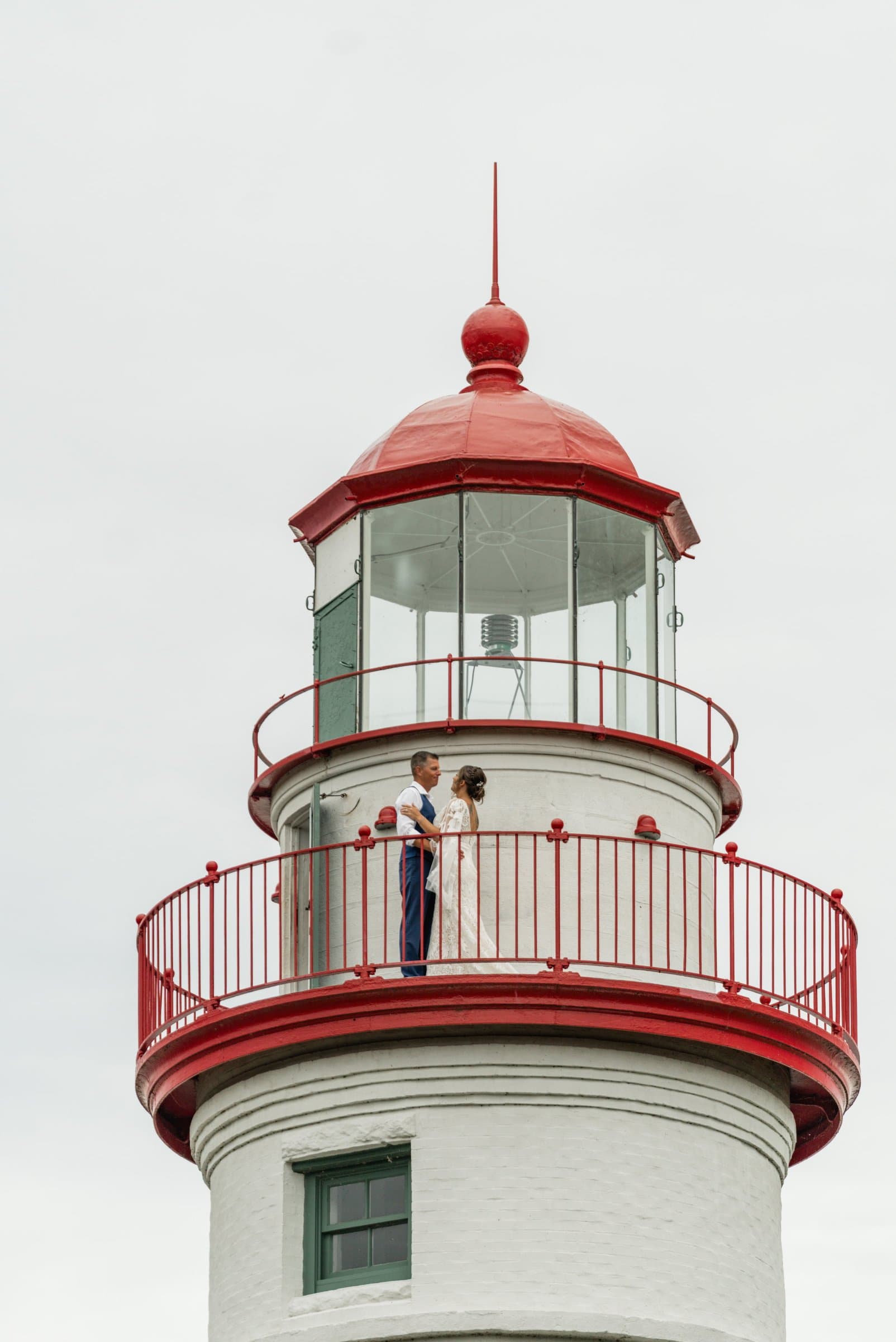 Newlyweds standing on the red railing gallery at the top of Marblehead Lighthouse