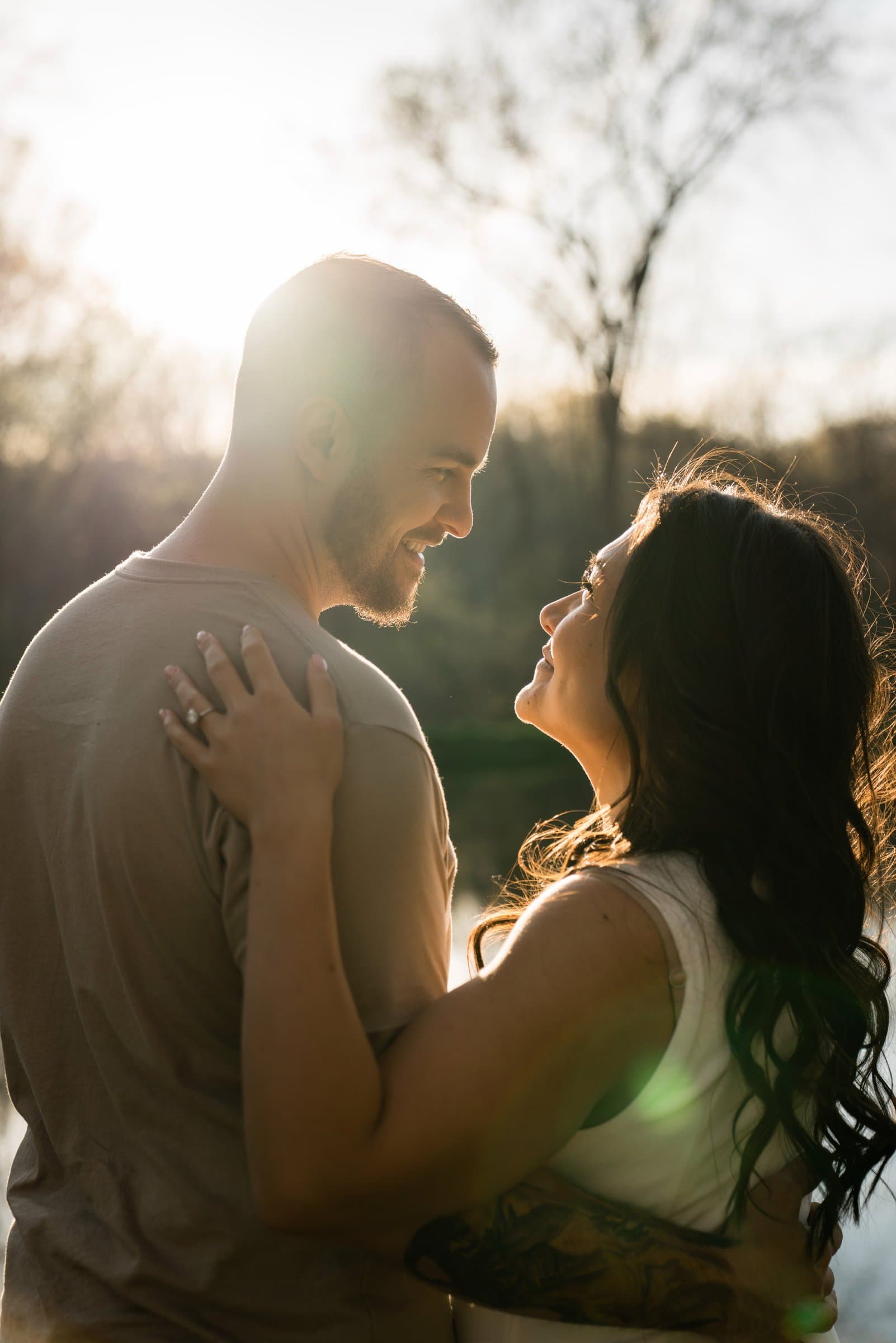 Couple laughing together in warm backlit sunlight during their engagement session