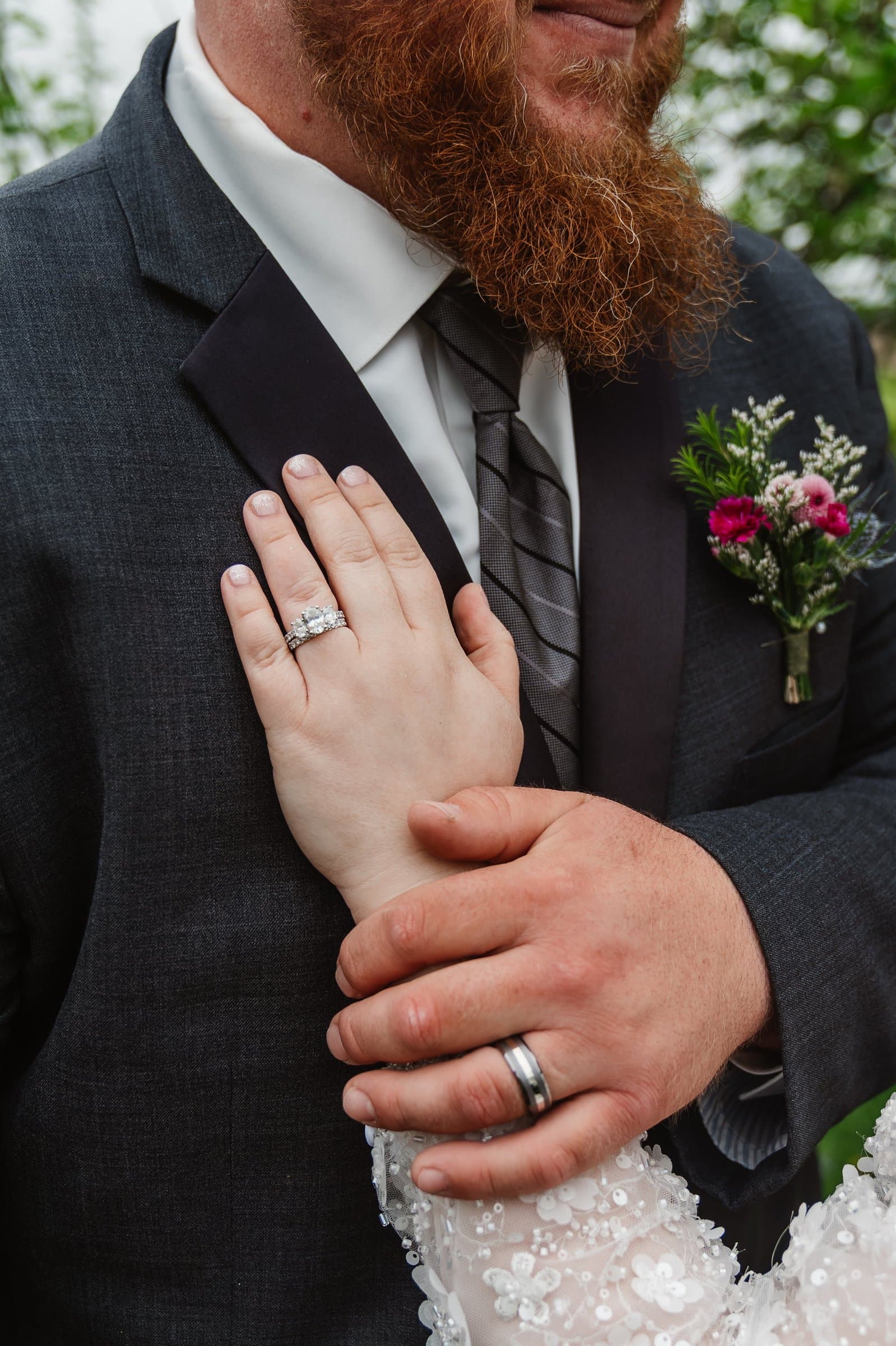 Newlyweds' hands showing their wedding rings against the groom's suit jacket