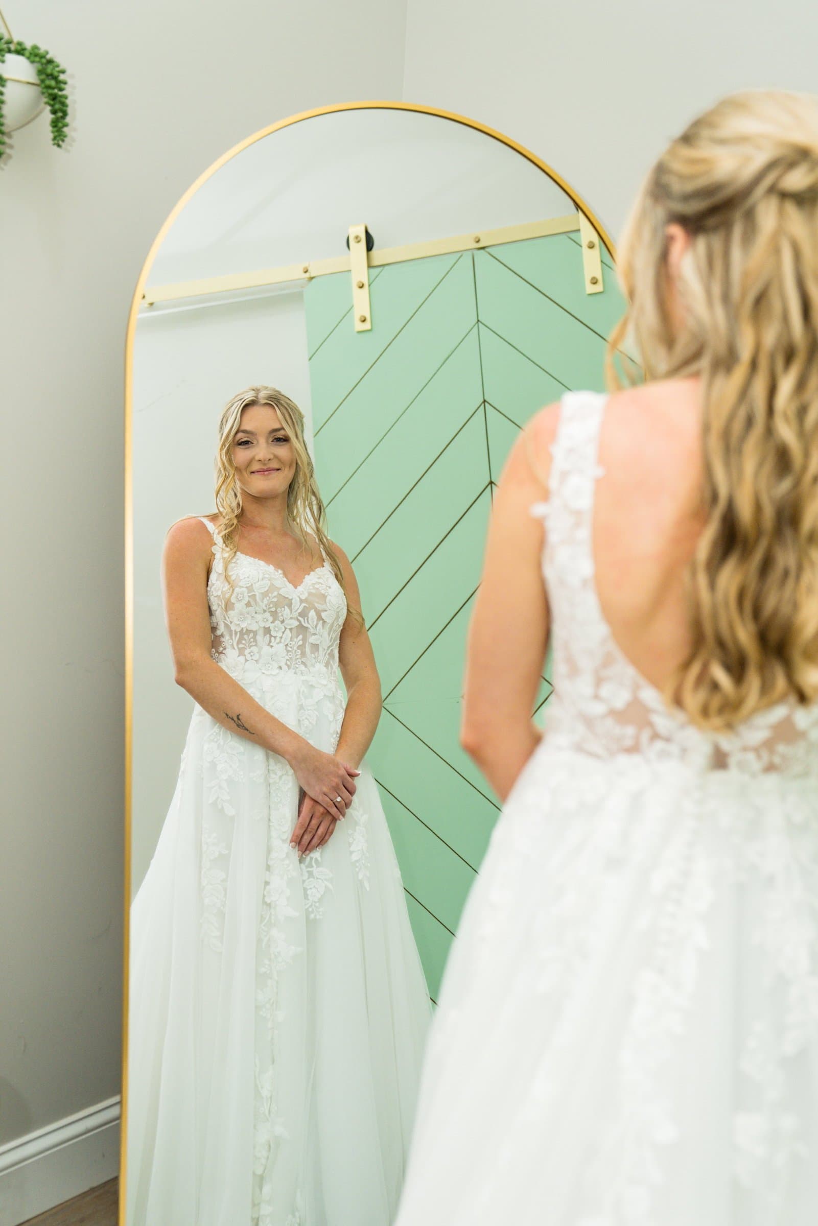 Bride in her wedding dress seen both directly and in a tall arched mirror while getting ready