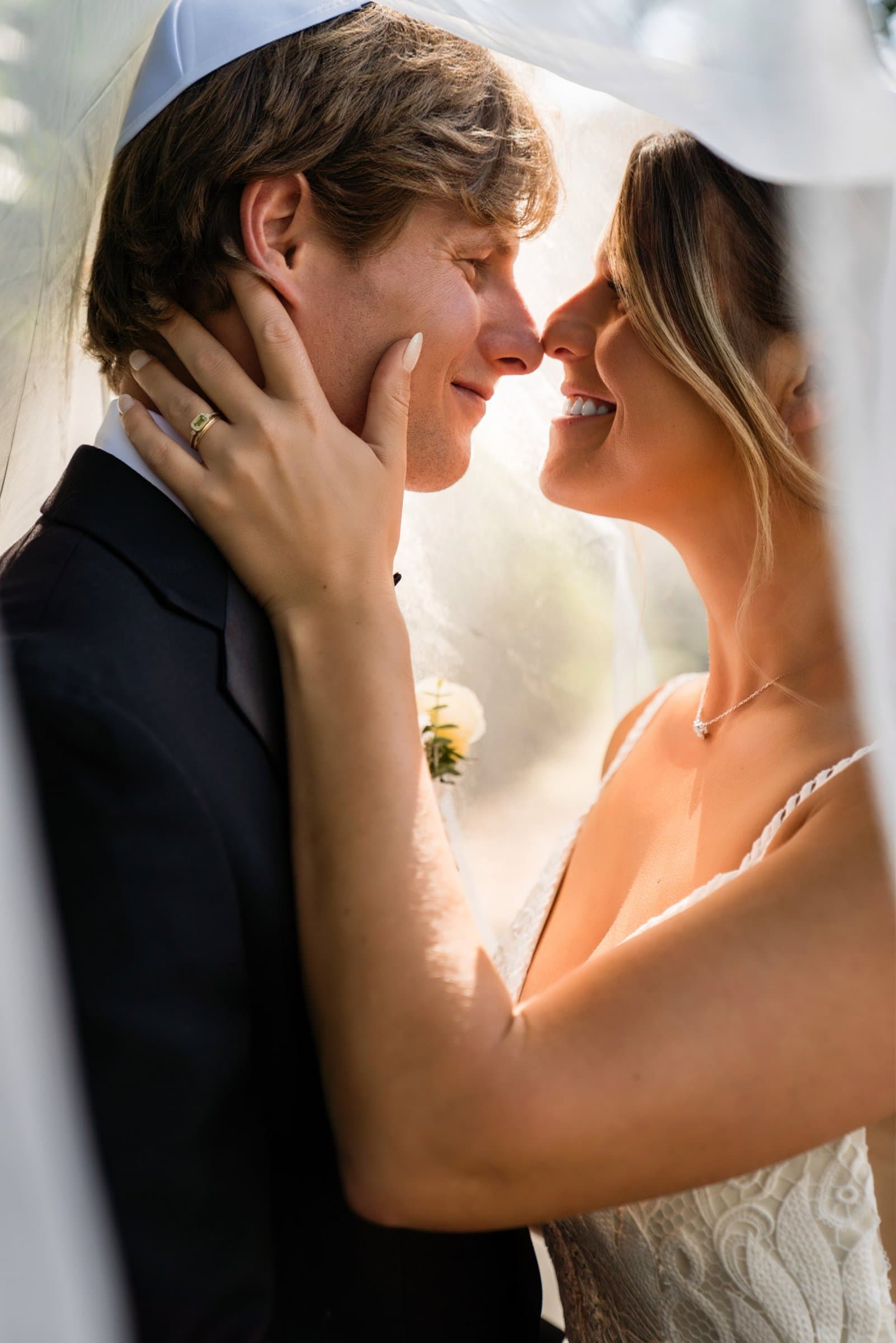 Bride holding her groom's face under her veil in a quiet moment together