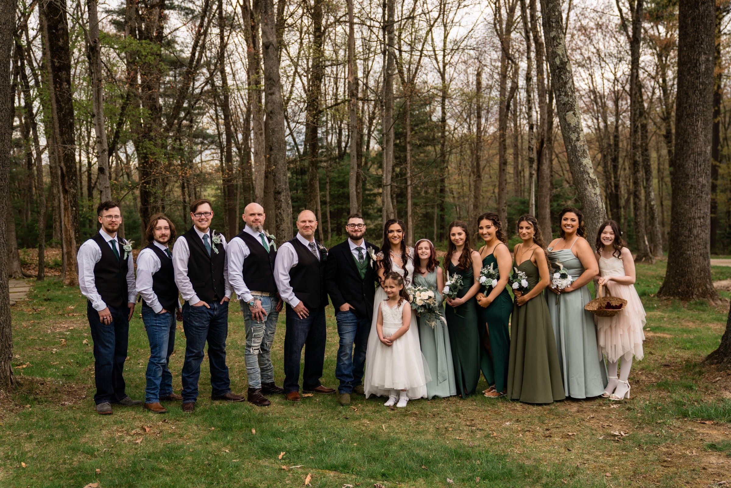 Full wedding party lined up for a group photo in a spring forest