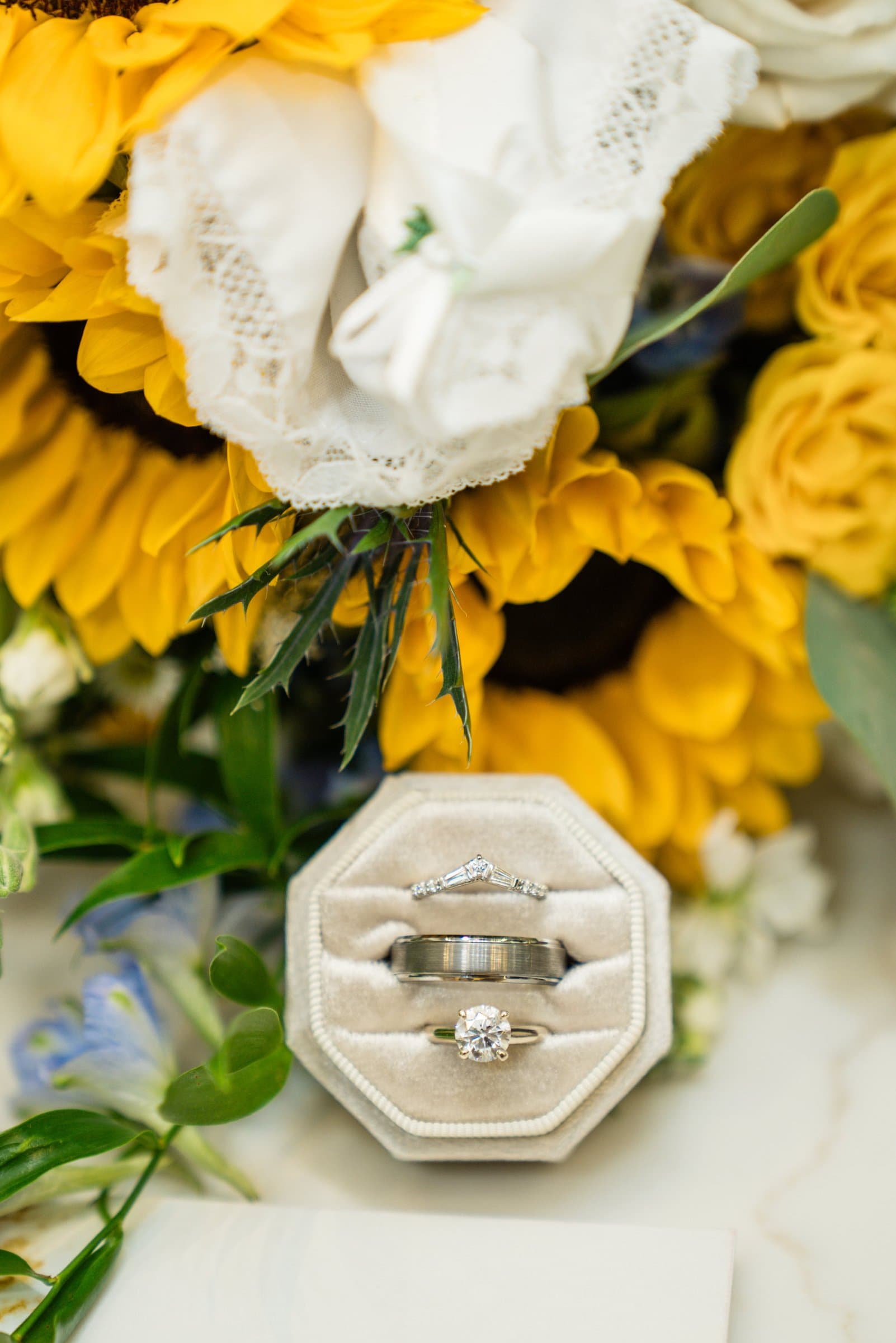 Wedding rings in a velvet ring box surrounded by sunflowers and white roses