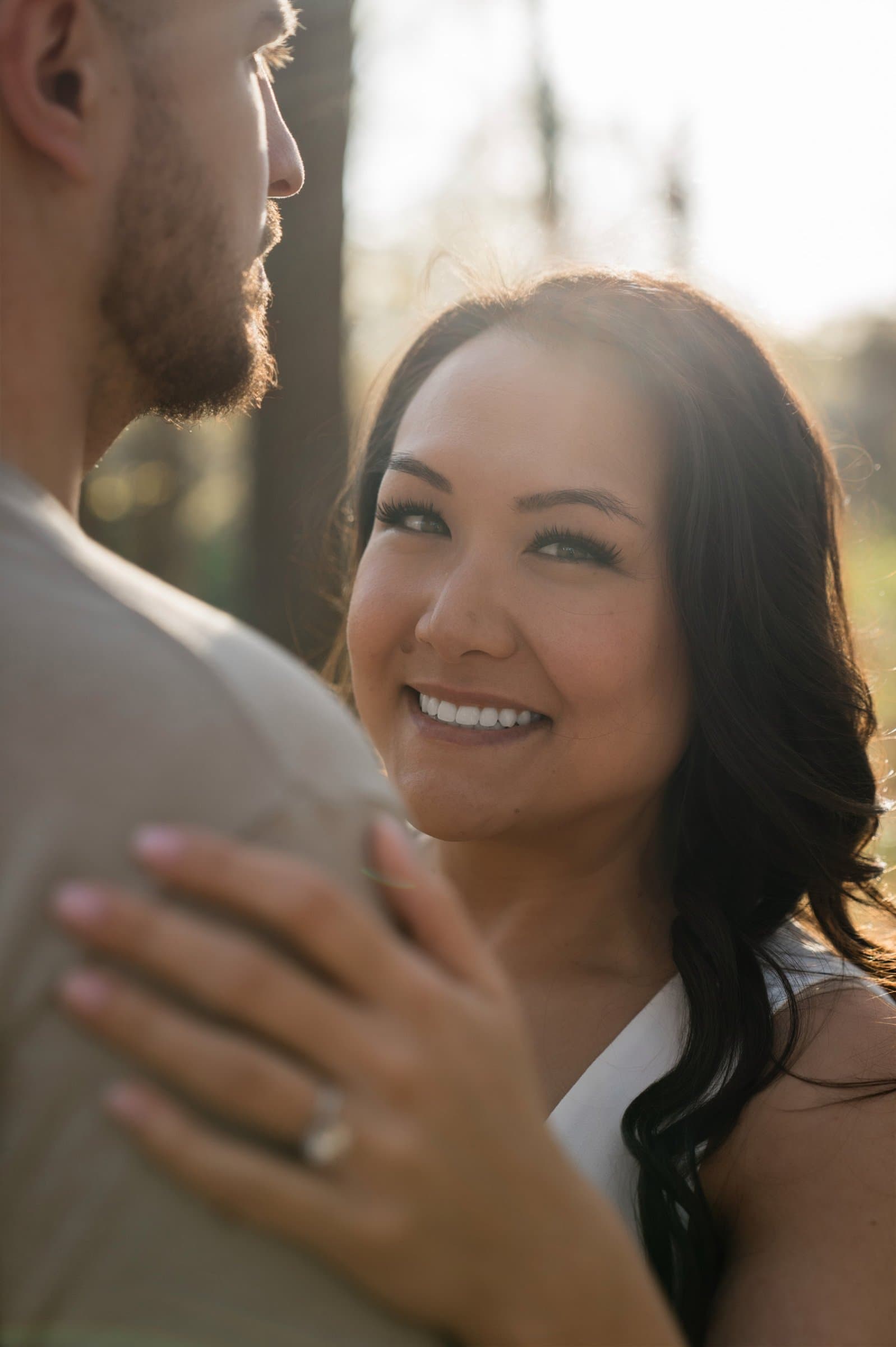 Smiling woman resting her hand with her engagement ring on her fiance's shoulder in golden light